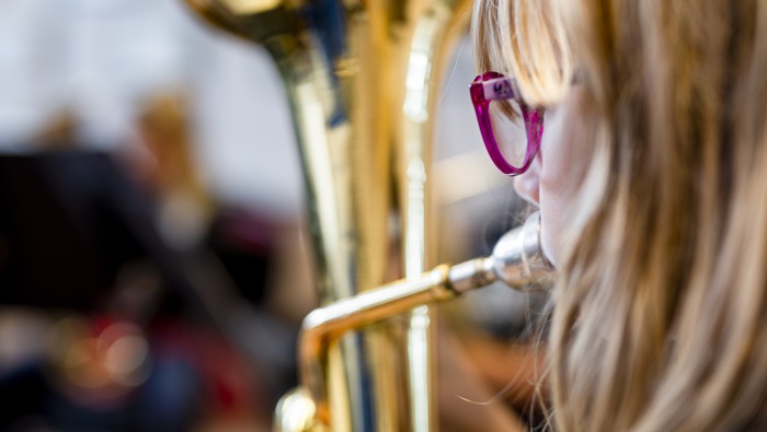 Närbild från sidan på flicka med rosa glasögon som spelar blåsinstrument