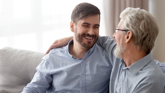 Cheerful 60s father embrace grown up child guy missed glad to see him, multi generational men relative people remembering life laughing, telling funny stories from past, dad and son connection concept