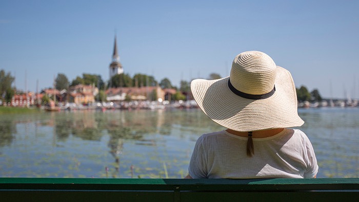 Kvinna med hatt på parkbänk vid vattnet i Mariefred.