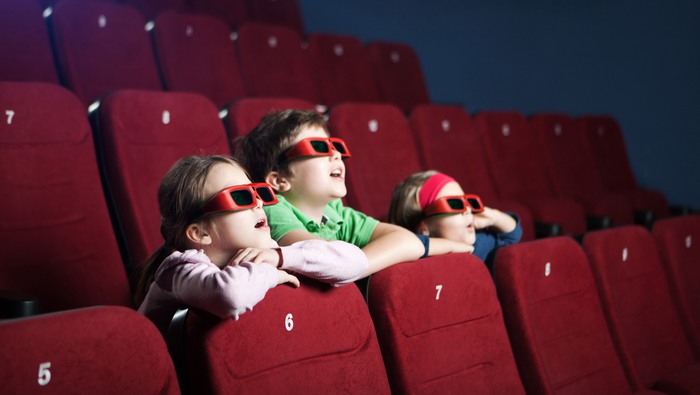 Tre barn som sitter i en biosalong och tittar på film.