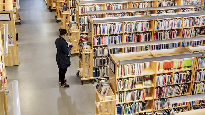 Kvinna läser en bok på ett bibliotek. 